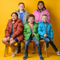 Five children wearing colorful bulk wholesale coats/jackets sitting on a bench against a yellow background